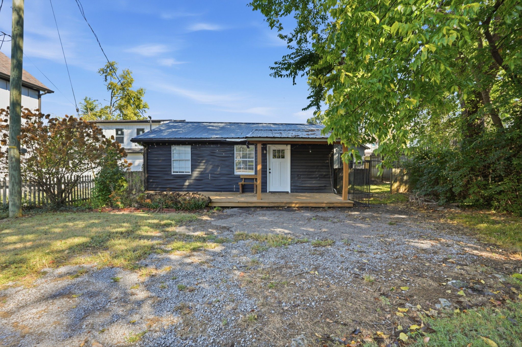 Street view of 1015 Spain Avenue, a small dark sided 1923 cottage with a white front door set back behind a gravel front yard, one of the East Nashville homes for sale in Nashville
