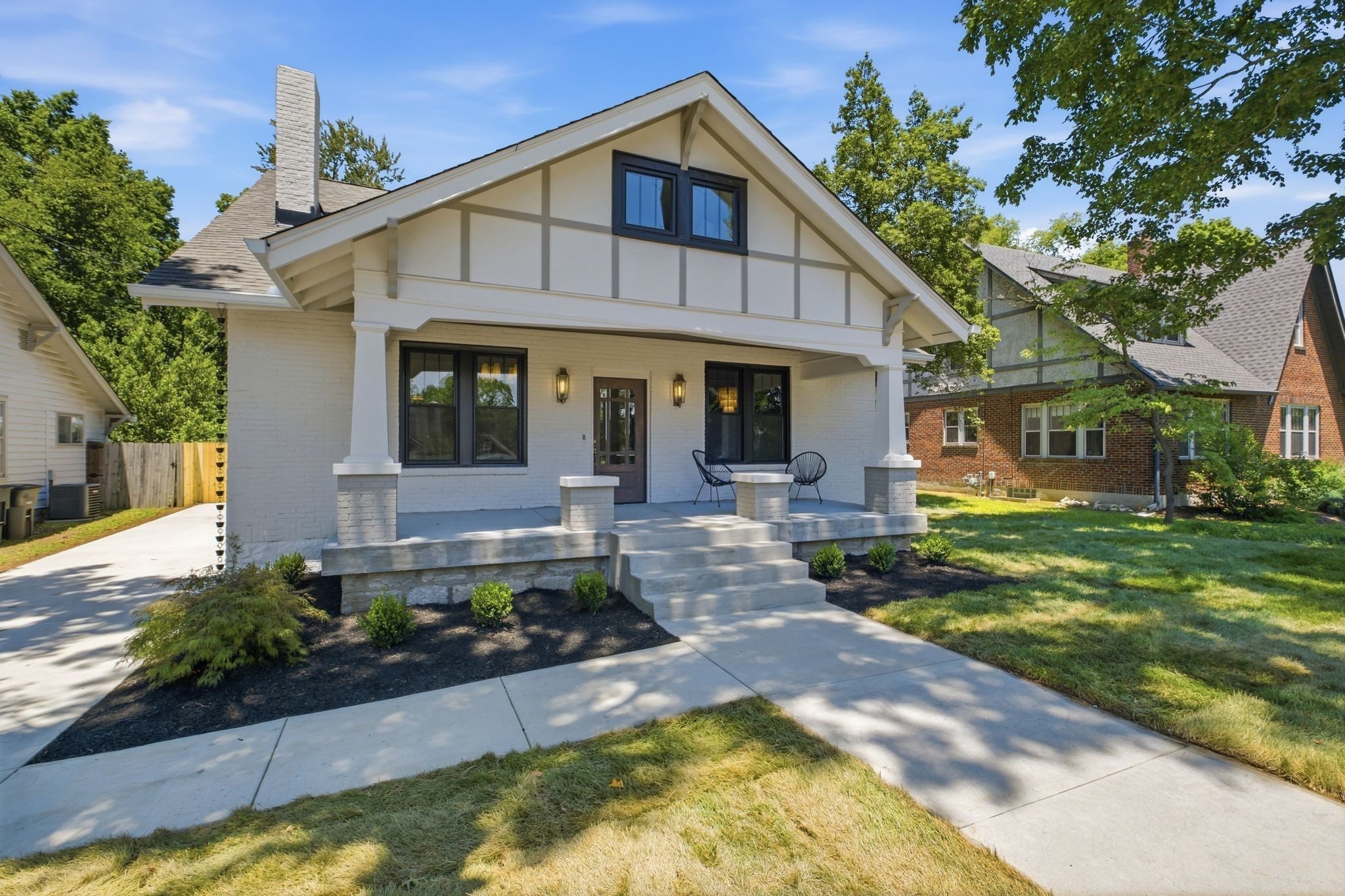 Front exterior of 1207 Shelton Avenue, a white 1925 bungalow with a front gable, black windows, a covered front porch with square columns, and a walk to the street, one of the East Nashville homes for sale in Nashville