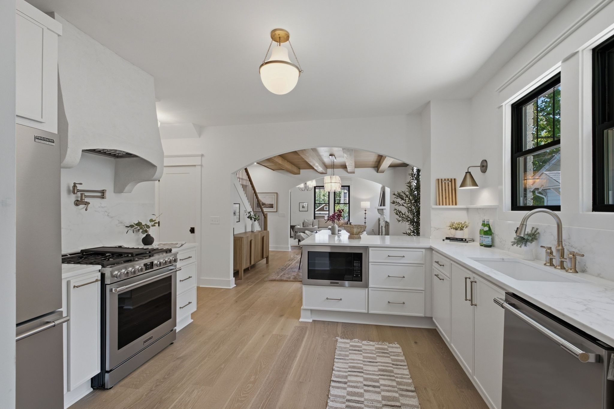 Kitchen with white cabinets, a plaster style range hood, stainless appliances, and light wood floors at 1207 Shelton Avenue in East Nashville
