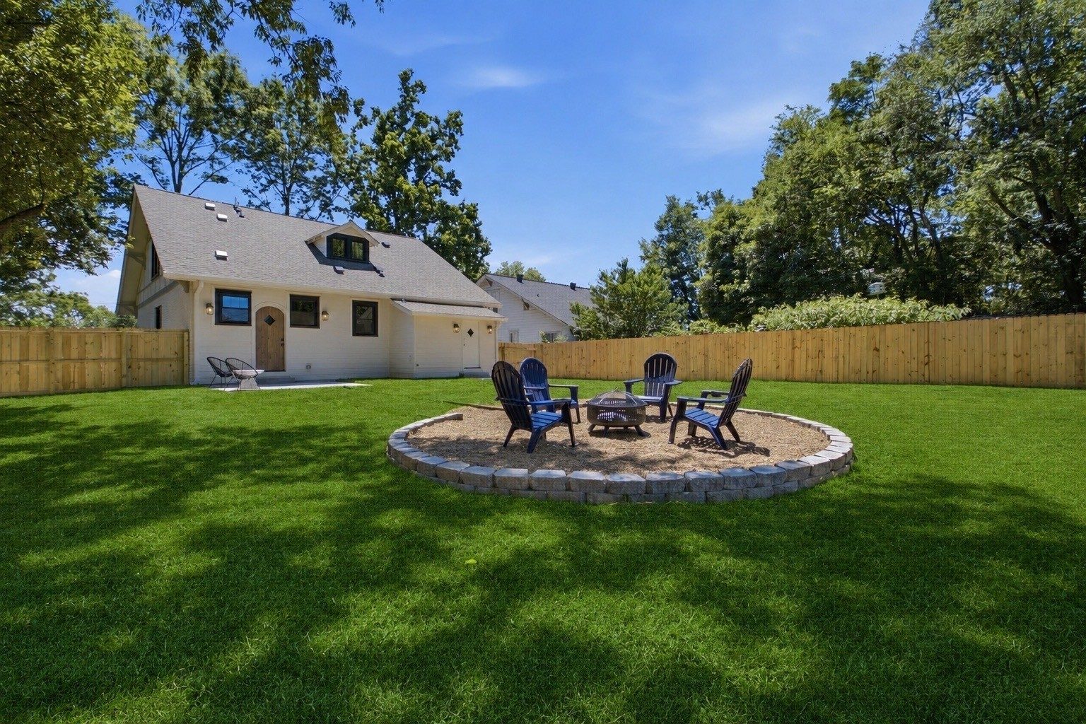 Fenced backyard with a lawn and a round stone fire pit with chairs at 1207 Shelton Avenue in East Nashville