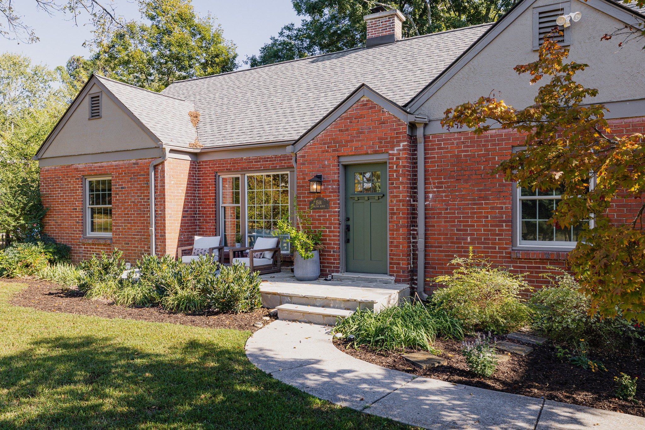 Front exterior of 1514 Shelton Avenue, a red brick 1948 bungalow with two front gables, a green front door, and a curved walk across the lawn, one of the East Nashville homes for sale in Nashville