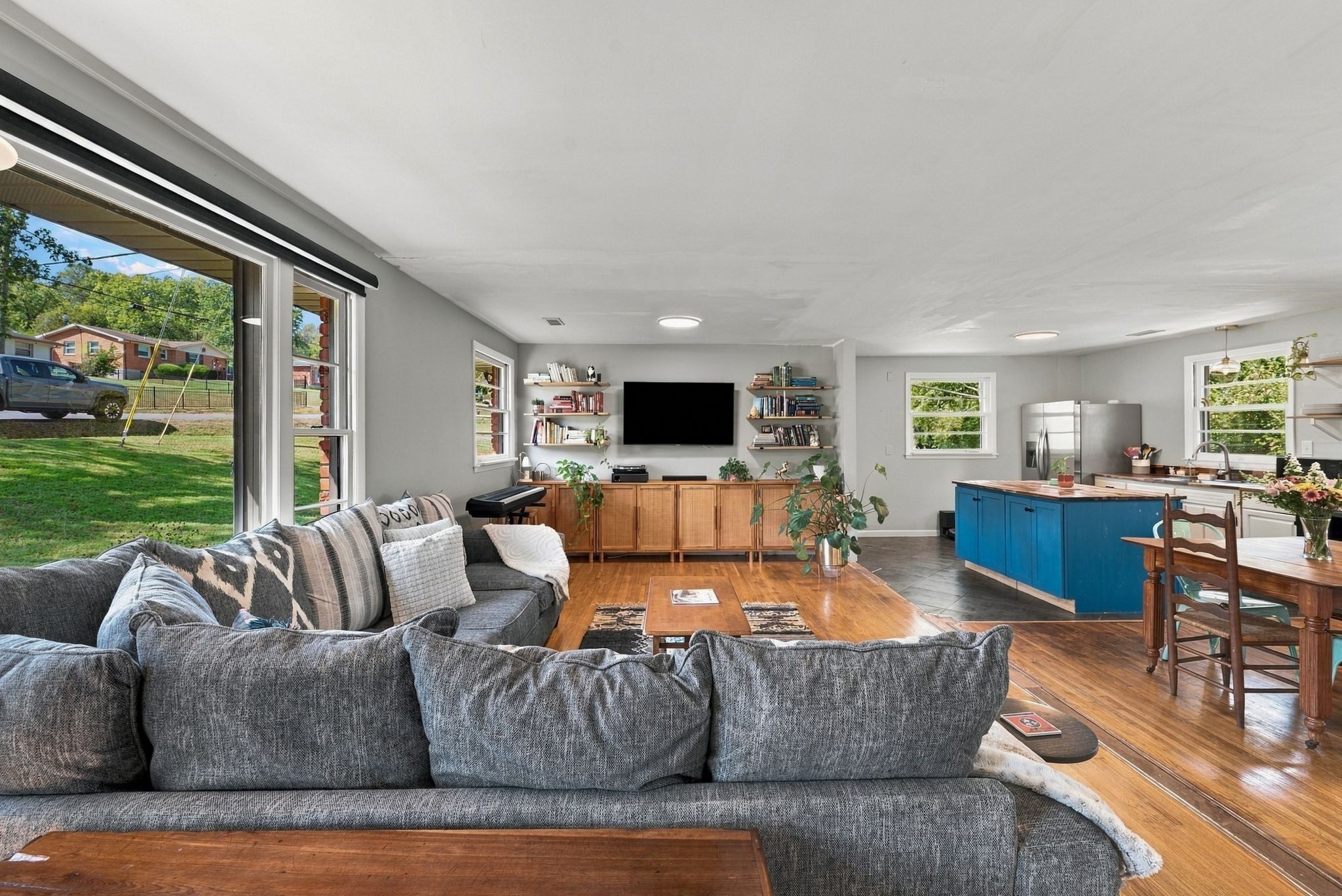Open living room with wood floors, a gray sectional, and a blue kitchen island in the background at 1829 Willow Springs Drive in East Nashville