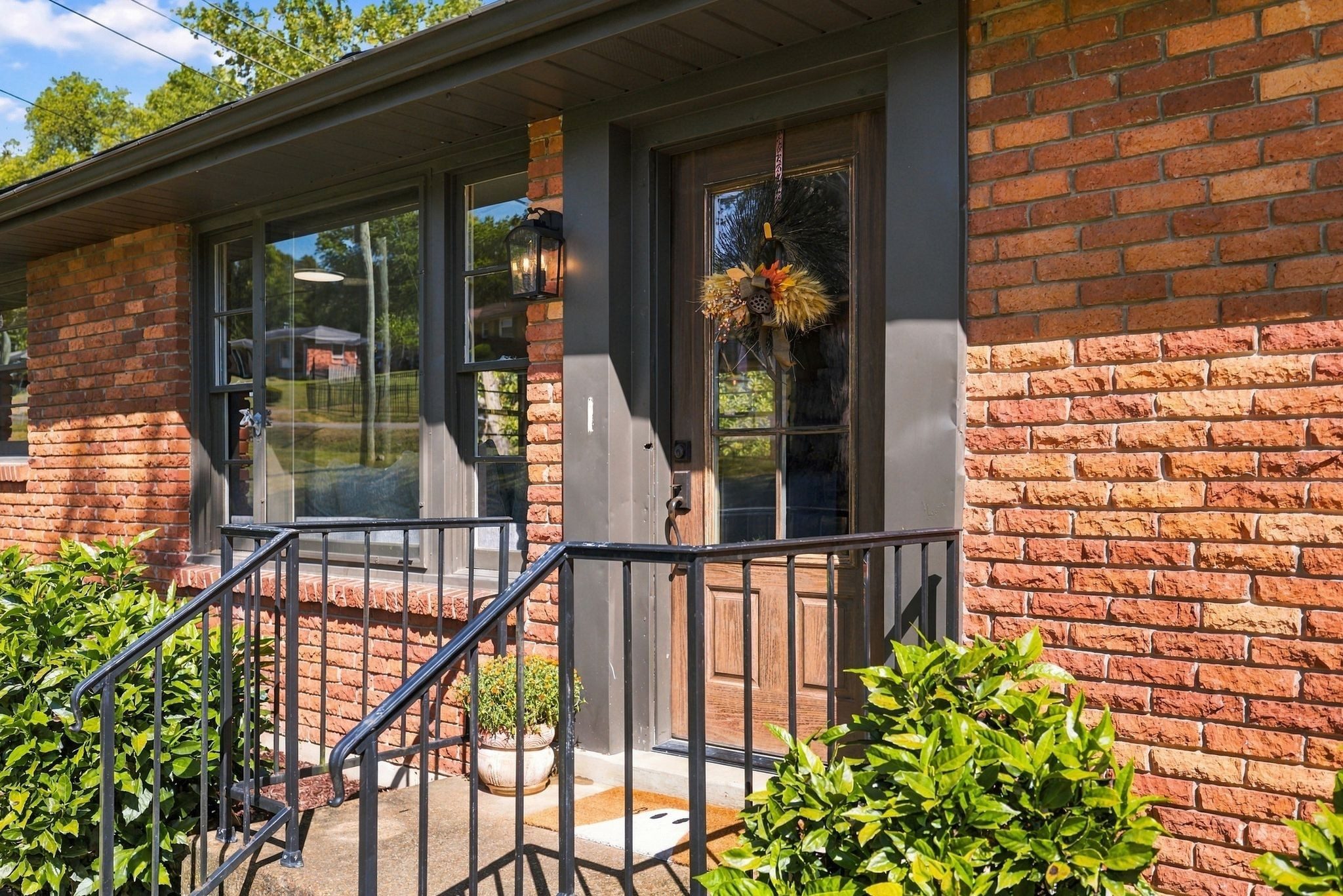 Front entry with dark trim, a wood front door, and black metal railings beside red brick at 1829 Willow Springs Drive in East Nashville