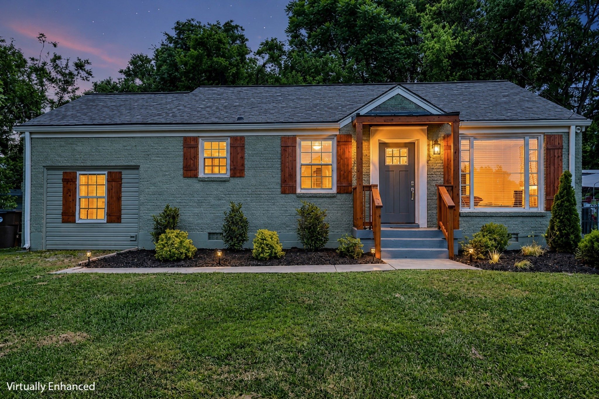 Front exterior of 2217 Pinewood Road at dusk, a one story painted brick home with red shutters, a cedar front porch, and a lit front window, one of the East Nashville homes for sale in Nashville