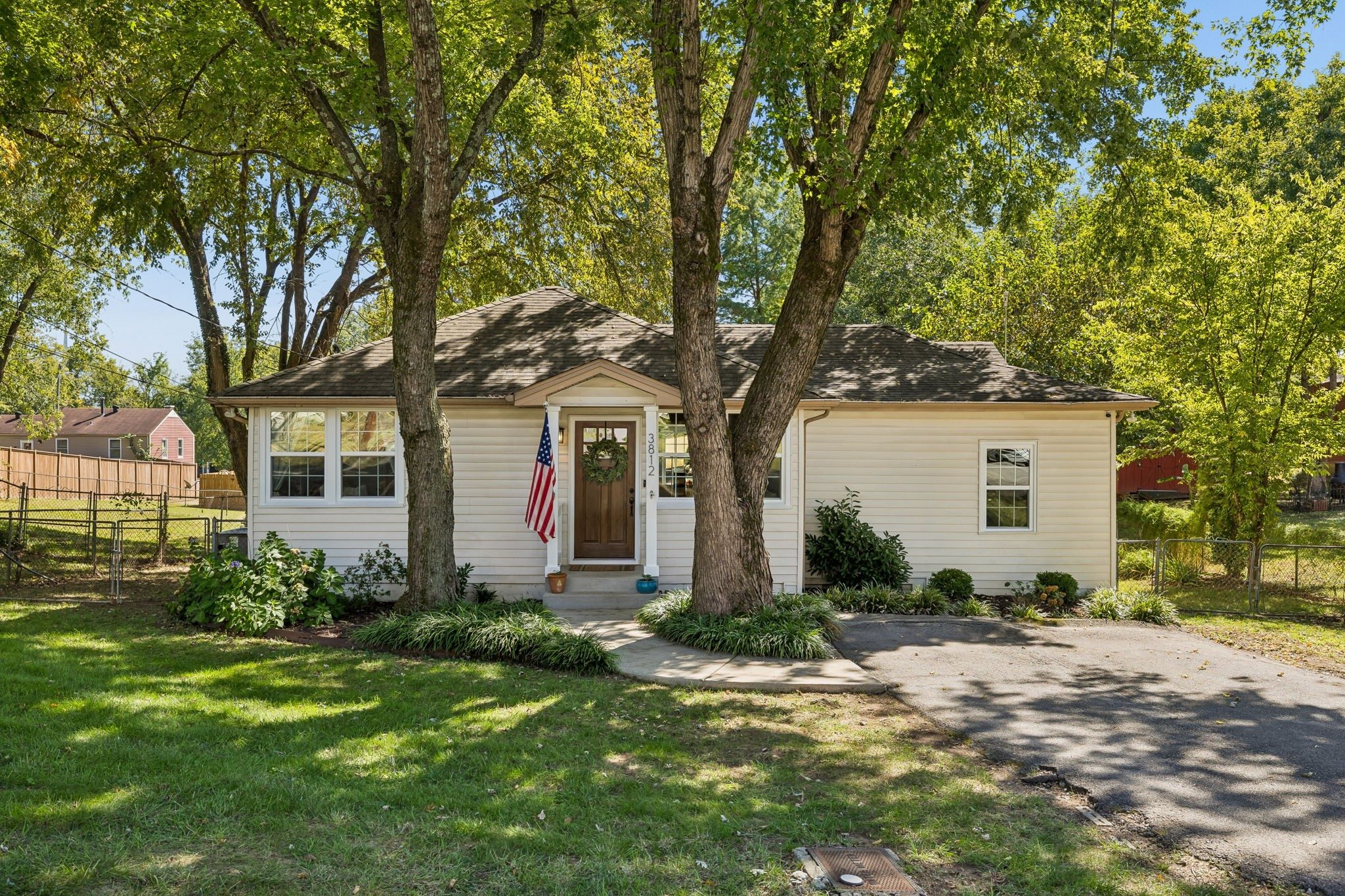 Front exterior of 3812 Inglewood Circle North, a white one story 1947 home with a wood front door, a small front gable, and large shade trees, one of the East Nashville homes for sale in Nashville