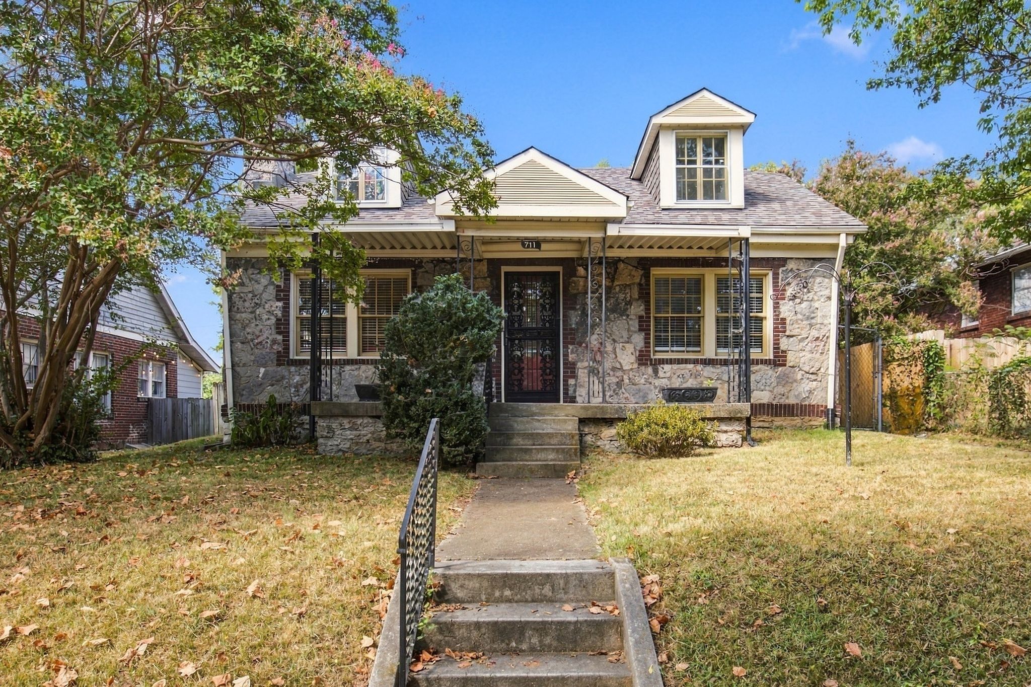 Front exterior of 711 Shelby Avenue, a 1920 stone bungalow with a front dormer, a covered front porch, and steps up from the sidewalk, one of the East Nashville homes for sale in Nashville